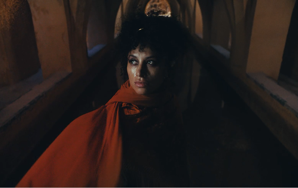 Woman wrapped in a red shawl standing beneath historic Andalusian arches, lit dramatically with a contemplative expression.