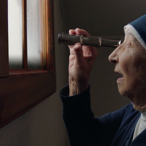Profile view of a nun using a telescope indoors, illuminated by soft natural light.