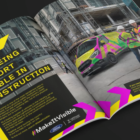 Wide-angle view of an open magazine displaying the Make It Visible campaign, showing construction scaffolding, workers in high-visibility gear, and bold campaign graphics.