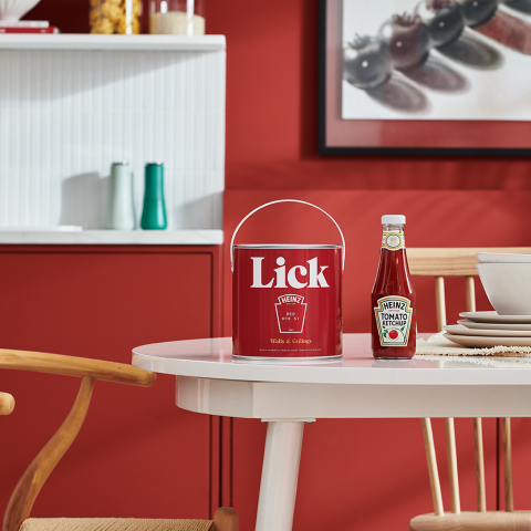 Woman painting a red wall using a roller beside a ladder, with Lick paint tins and Heinz Tomato Ketchup styled in a studio setting.