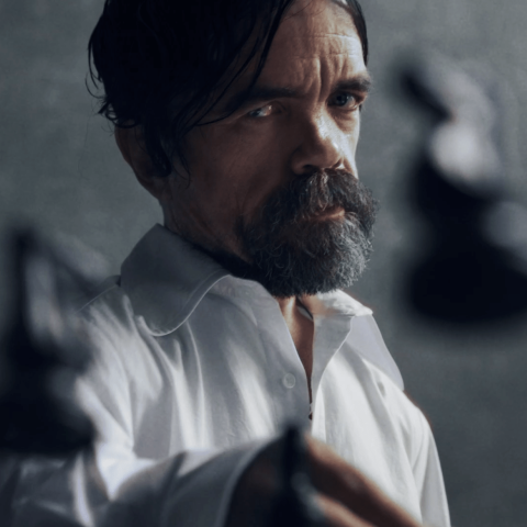 Man in a white shirt holding chess pieces, symbolising strategy and intensity against a dark, minimalist background.