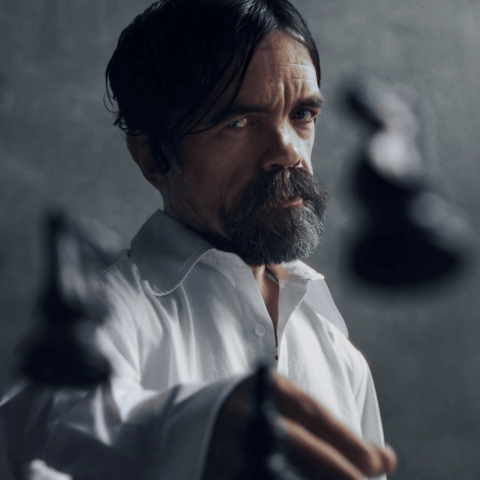 Man in a white shirt holding chess pieces, symbolising strategy and intensity against a dark, minimalist background.