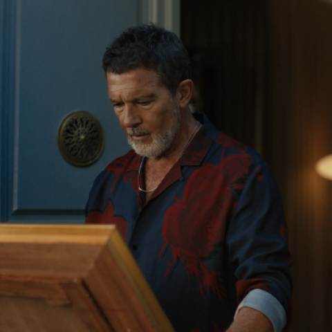 Antonio Banderas standing in a doorway looking at a framed painting while wearing a dark patterned shirt in the Goya campaign.