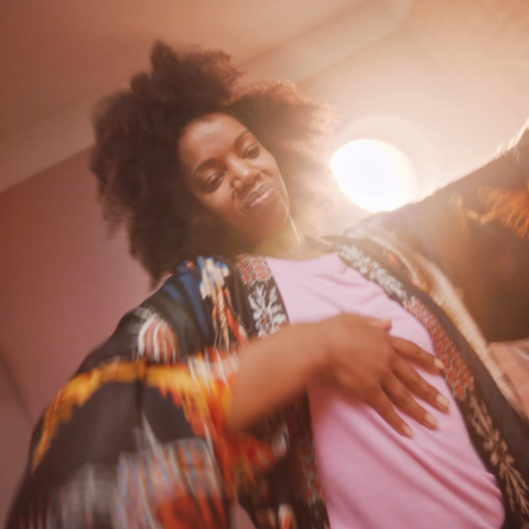 Woman smiling and moving confidently while wearing patterned robe during self-care routine.