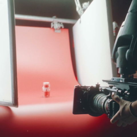 Behind-the-scenes studio setup filming a Coca-Cola can against a red background with professional camera equipment.
