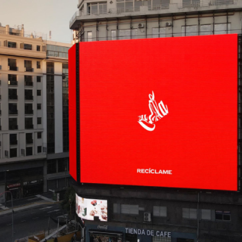 Large Coca-Cola Recycle Me billboard glowing red on the side of a city building.