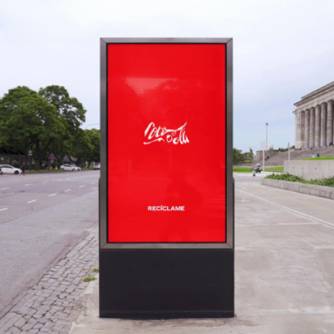 Coca-Cola Recycle Me message displayed on a tall outdoor digital billboard in an urban setting.