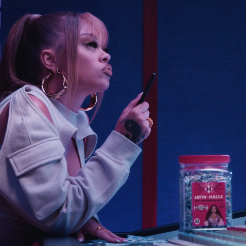 Wide shot of a woman working in a recording studio with audio equipment and a jar of Halls lozenges on the desk.