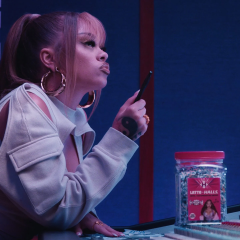 Woman sitting at a recording studio desk holding a pen, with a jar of Halls lozenges placed in front of her.
