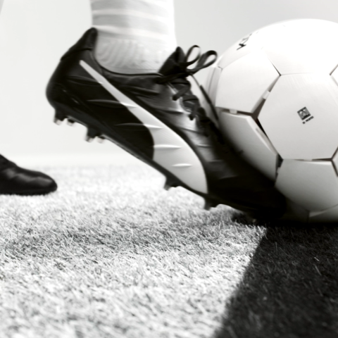 Black football boot representatively controlling a LaLiga football on artificial turf with a field line visible.